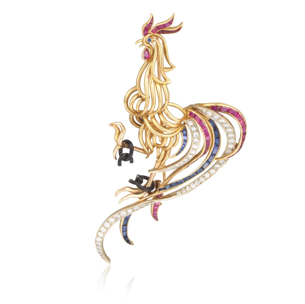 BROCHE 'COQ' SAPHIRS, RUBIS ET DIAMANTS: BROCHE 'COQ' SAPHIRS, RUBIS ET DIAMANTS Formant un coq stylisé brisant ses chaînes en or émaillé noir avec ses pattes, son oeil serti d'un saphir de forme ronde, sa crête et s