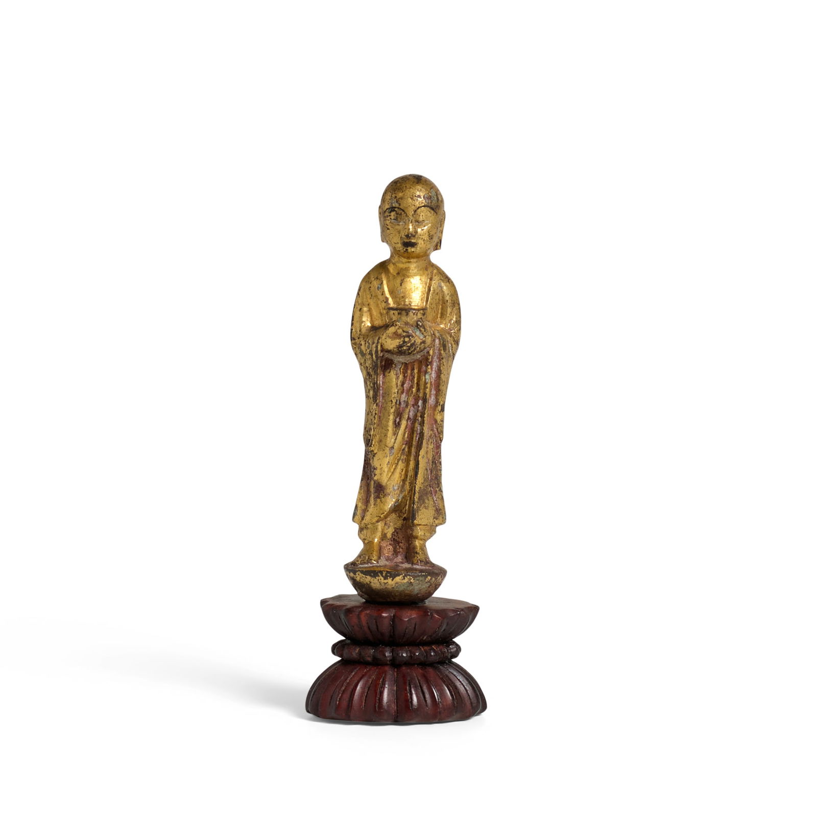 A SMALL GILT BRONZE FIGURE OF A BUDDHIST DISCIPLE Tang Dynasty: A SMALL GILT BRONZE FIGURE OF A BUDDHIST DISCIPLE Tang Dynasty The youthful face with a contemplating gaze, standing with both hands holding an alms bowl at the chest, wearing a simple kasaya with ple
