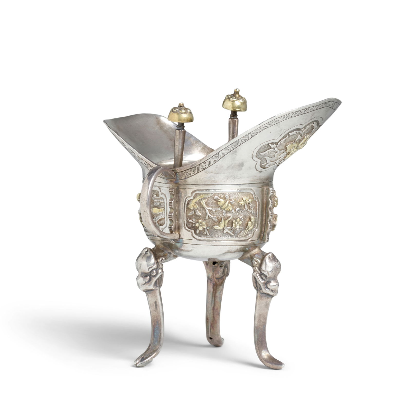 AN EARLY QING ARCHAISTIC SILVER AND GILT TRIPOD LIBATION CUP 17th/18th century: AN EARLY QING ARCHAISTIC SILVER AND GILT TRIPOD LIBATION CUP 17th/18th century The vessel of usual cup-shape with a large and a small petal-shaped flanges rising from the rim with two posts with dome