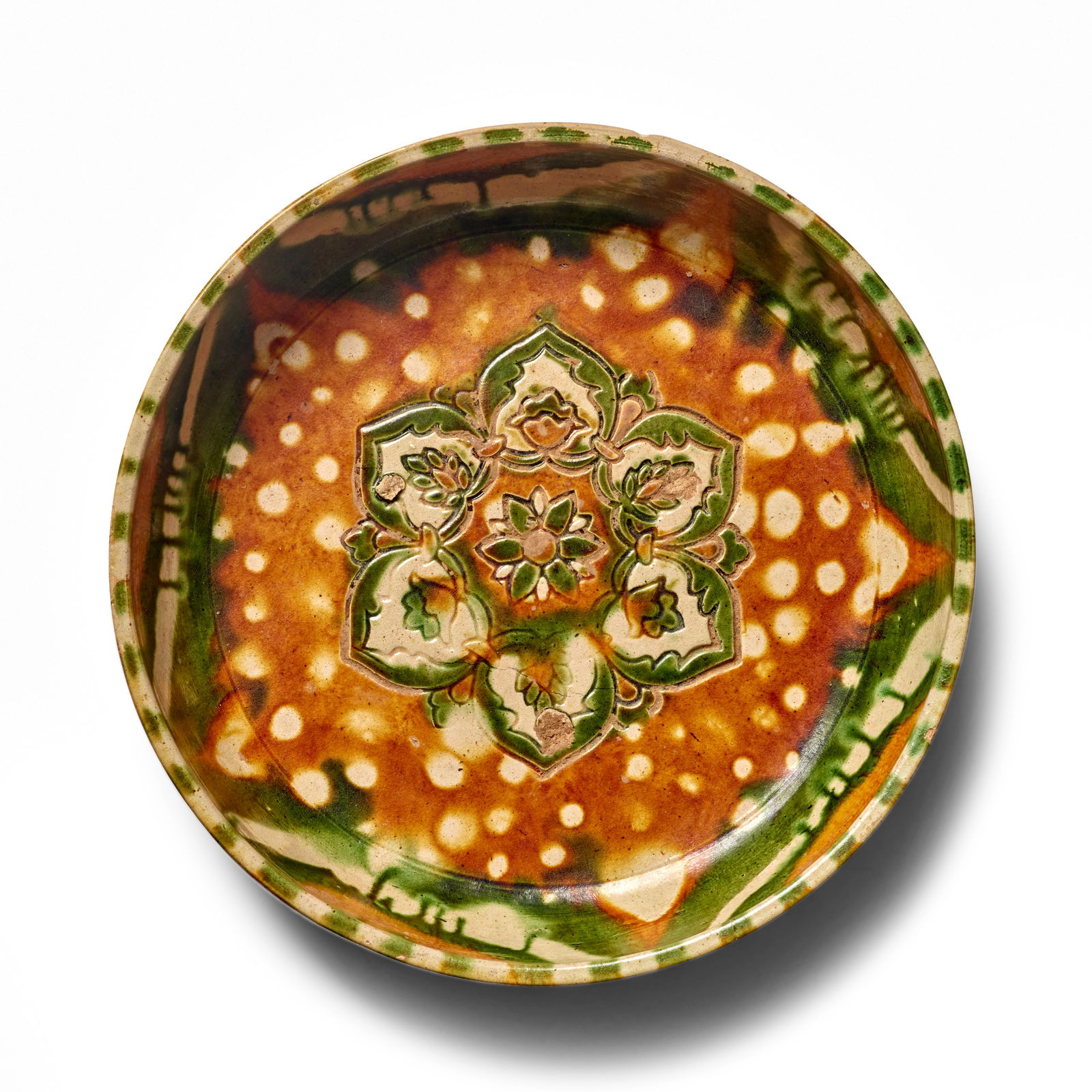 A SANCAI-GLAZED POTTERY SHALLOW BOWL Tang Dynasty: A SANCAI-GLAZED POTTERY SHALLOW BOWL Tang Dynasty The floral medallion of green and ocher at the center surrounded by an ocher ground with wax-resisted spots, the interior wall with five freely painte