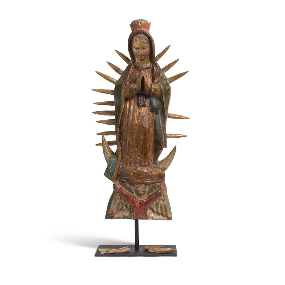A Mexican bulto depicting Our Lady of Guadalupe: A Mexican bulto depicting Our Lady of Guadalupe Circa 1870, depicted standing with hands together in prayer, a crown above her head and gilt rays radiating from her body, surmounting an angel with arm