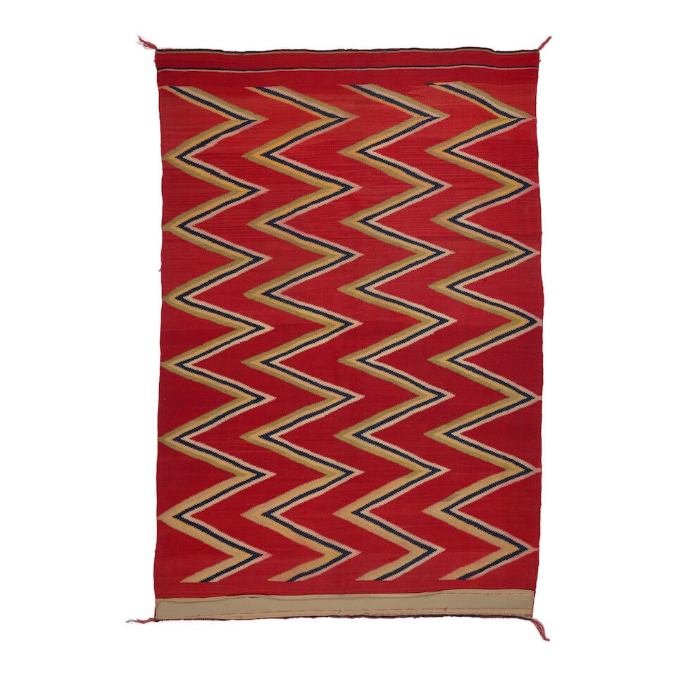 A Diné (Navajo) late classic serape: A Diné (Navajo) late classic serape Worked with multi-colored zigzag bands in indigo, vegetal green and yellow, and cream overlaid on a red ground, with thin bands at each end. size approximately