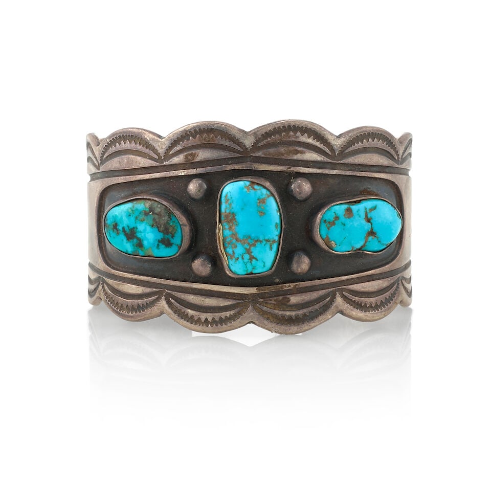 A Diné (Navajo) cuff bracelet: A Diné (Navajo) cuff bracelet A silver cuff of scalloped outline, stamped and set with three turquoise stones, with silver drop accents. inner circumference (including gap) 6 1/4in, gap 13/16in,