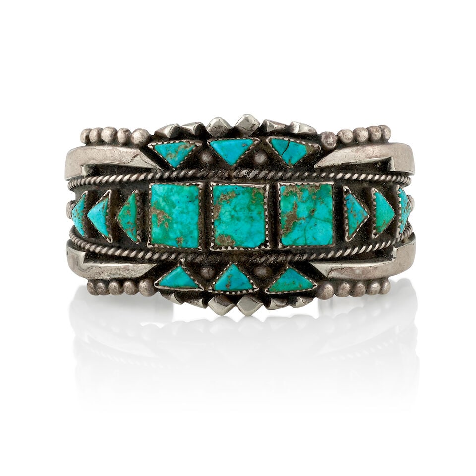 A Diné (Navajo) or Zuni cuff bracelet: A Diné (Navajo) or Zuni cuff bracelet A heavy example, set with rectangular and triangular turquoise within a deep relief surround with silver drop and twisted wire accents. inner circumference
