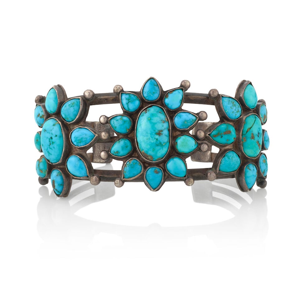 A Diné (Navajo) or Zuni cuff bracelet: A Diné (Navajo) or Zuni cuff bracelet A large example, constructed of two carinated and one rounded wire supporting flower-like arrangements of turquoise, with silver drop accents. inner