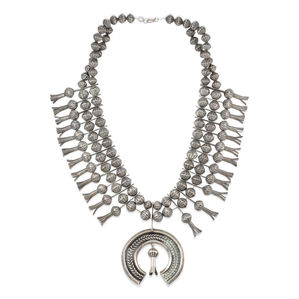 A Diné (Navajo) squash blossom necklace: A Diné (Navajo) squash blossom necklace A heavy example, designed with two strands of fluted silver beads strung with 24 conforming three-petal blossoms and suspending a large carinated and