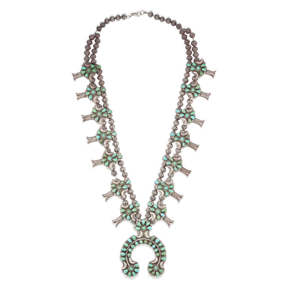 A Diné (Navajo) squash blossom necklace: A Diné (Navajo) squash blossom necklace Likely the work of Mary and Tsosie Taylor, designed with two strands of fluted silver beads strung with 14 blossoms set with Castle Dome turquoise and a