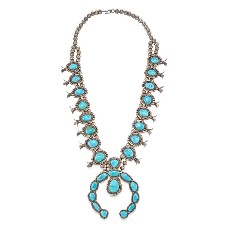 A Nellie Bain squash blossom necklace: Nellie Bain Diné (Navajo), (20th/21st century), a silver squash blossom necklace set with Morenci turquoise, constructed of a single branching to a double strand of silver beads strung with 16