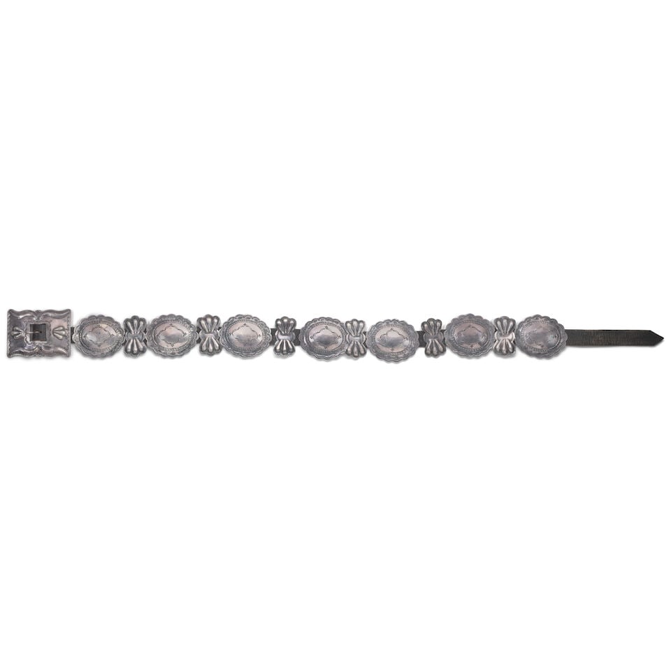 A Southwest silver concho belt: A Southwest silver concho belt Designed with seven stamped oval conchas with scalloped edges separated by six repoussé-decorated bowtie or butterfly spacers, with a rectangular stamped and