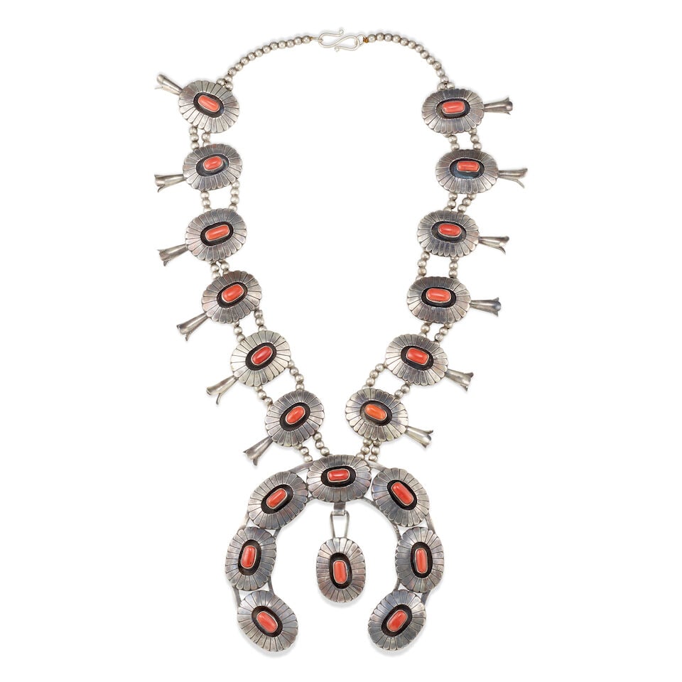 A Diné (Navajo) squash blossom necklace: A Diné (Navajo) squash blossom necklace Designed with a single branching to a double strand of petite silver beads, strung with twelve shadowbox-style blossoms set with coral and suspending a lar