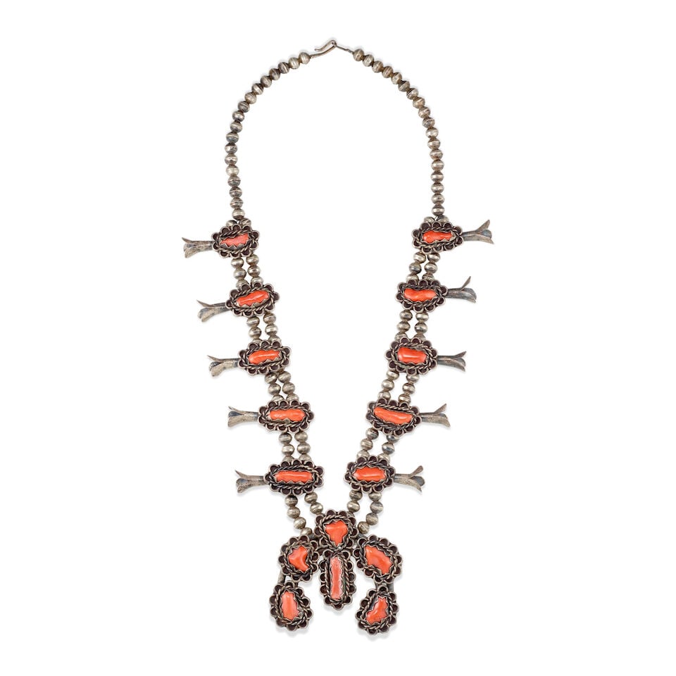 A Diné (Navajo) squash blossom necklace: A Diné (Navajo) squash blossom necklace Designed with a single branching to a double strand of silver beads strung with ten graduated blossoms set with coral, the conformingly designed naja set w