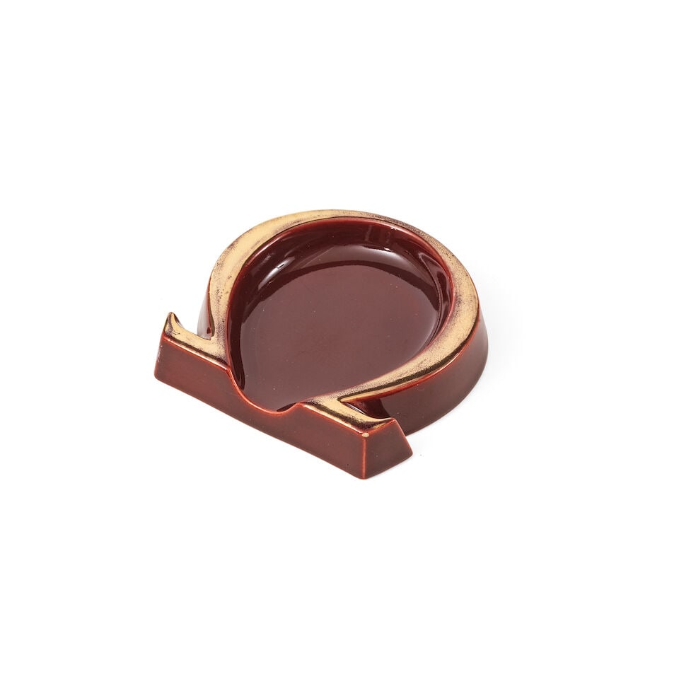 Omega. A burgundy glazed ceramic ashtray in the form of the Omega logo Omega. Cendrier bordeaux ...: Omega. A burgundy glazed ceramic ashtray in the form of the Omega logo Omega. Cendrier bordeaux en ceramique émaillé dans la forme du logo Omega 11cm x 10.5cm Two noticeable chips to the