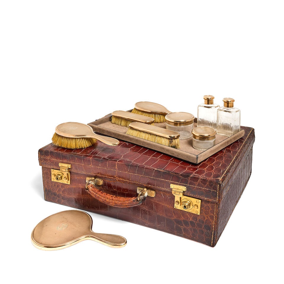 A 9 carat gold nine-piece dressing set with a crocodile covered travelling case Asprey & Co Ltd,...: A 9 carat gold nine-piece dressing set with a crocodile covered travelling case Asprey & Co Ltd, London 1929, also stamped ASPREY LONDON The set with engine-turned surface within bead and husk banded 