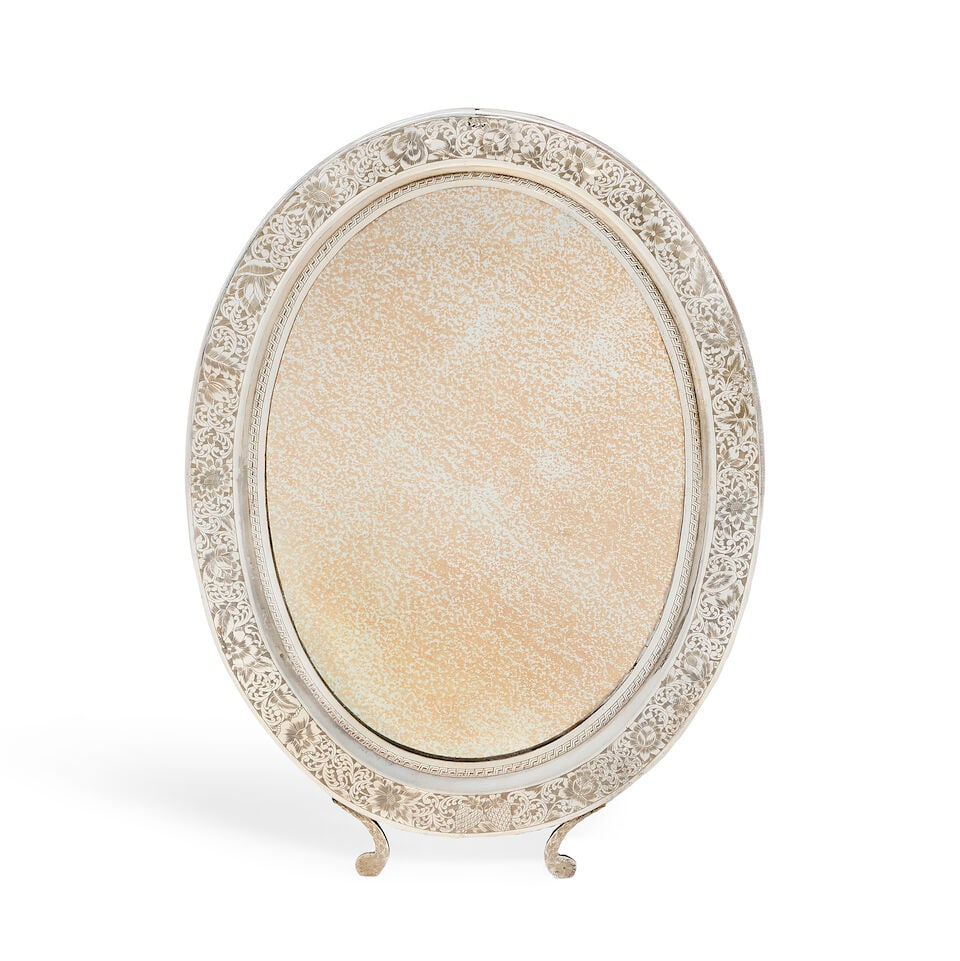 A Middle Eastern silver mirror maker's mark stamped VIGE, stamped 84: A Middle Eastern silver mirror maker's mark stamped VIGE, stamped 84 Oval form, with foliate engraved decoration, with two scroll supports, with wooden backing and support, height 46cm. For further in