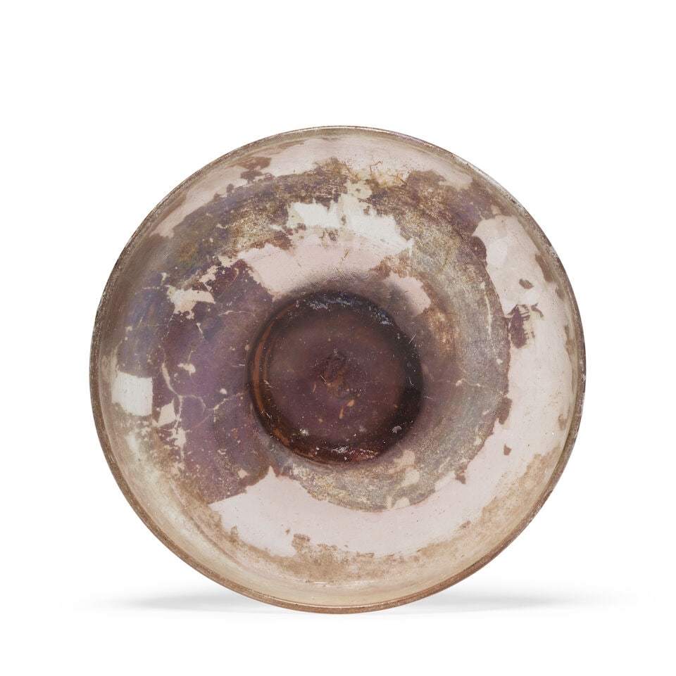 A Roman pale streaky purple glass dish: A Roman pale streaky purple glass dish Circa 4th Century A.D. 14.7cm diam. Footnotes: Provenance: with Charles Ede Ltd., London (Roman Glass XI, 1986, no. 15). Private collection, UK, acquired from