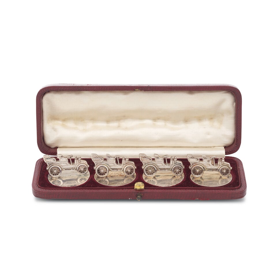 A cased Edwardian set of four sterling silver 'motor car' menu/place card holders: A cased Edwardian set of four sterling silver 'motor car' menu/place card holders bearing the mark of John Collard Vickery overstriking that of another, London 1905, each modelled as a vintage car mou