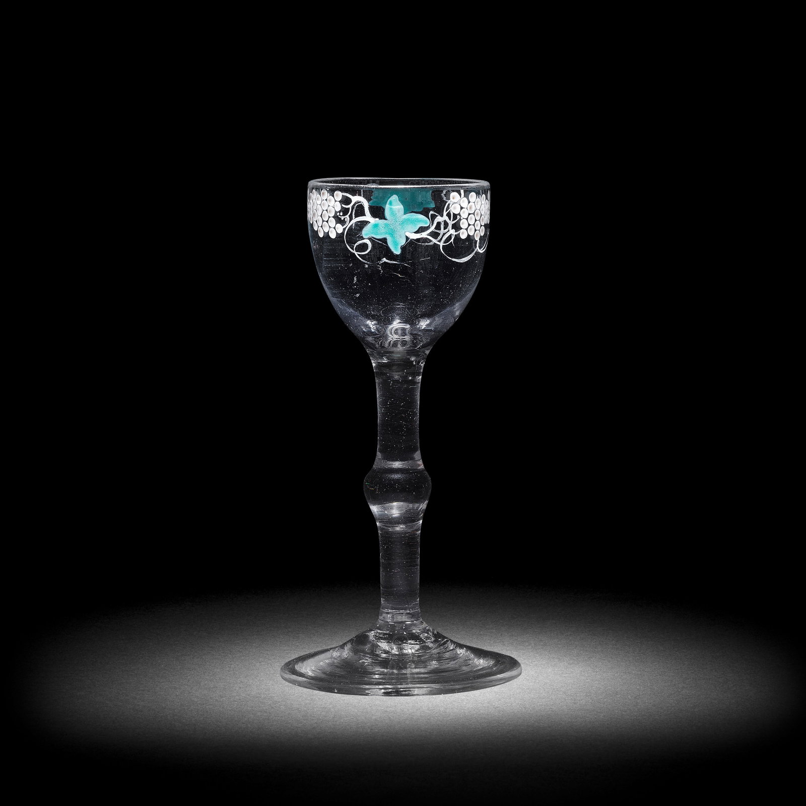 A fine Beilby polychrome enamelled baluster wine glass, circa 1765: A fine Beilby polychrome enamelled baluster wine glass, circa 1765 The cup-shaped bowl painted with a border of fruiting vine in opaque white, the leaves in opaque turquoise, the rim with traces of gi
