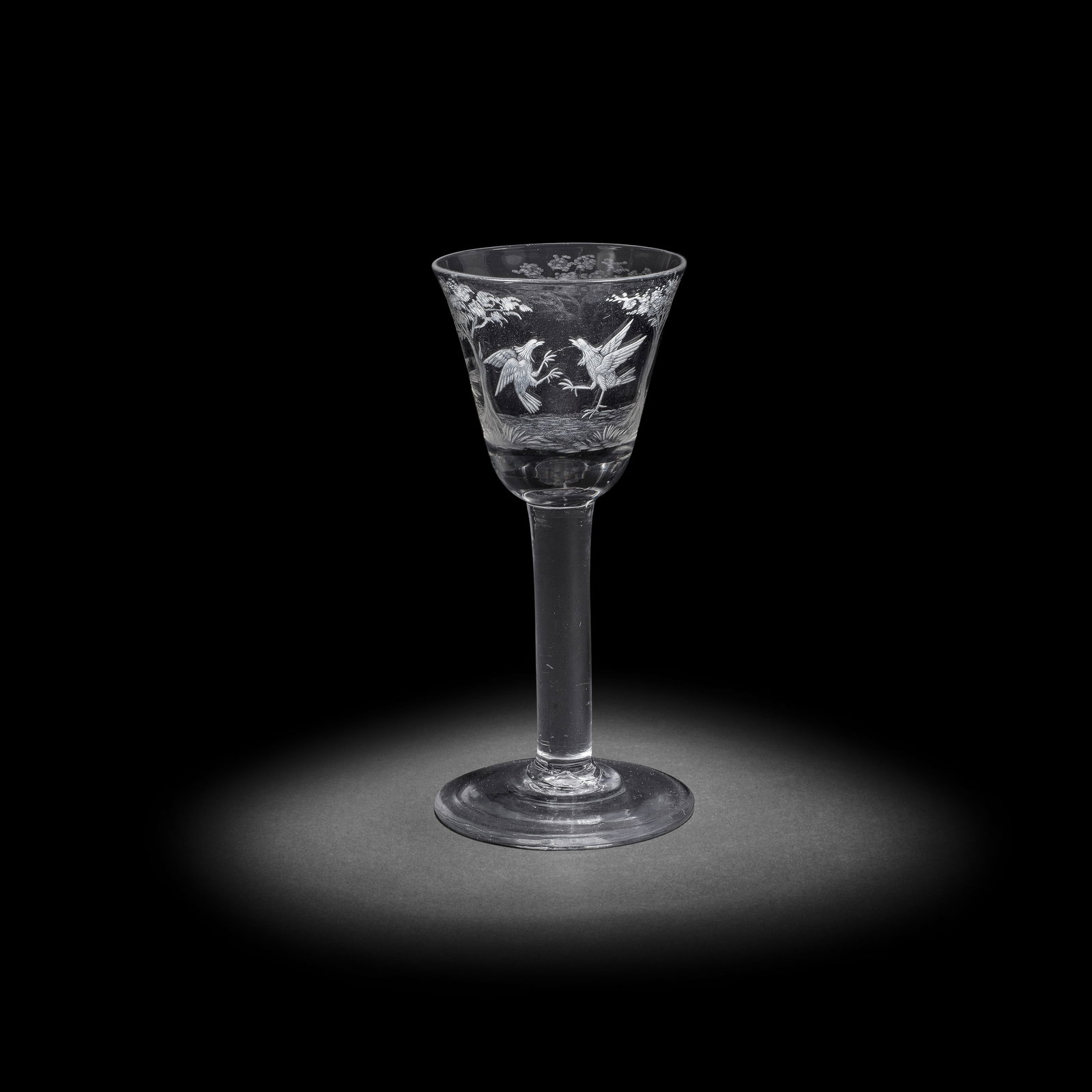 A rare engraved cockfighting wine glass, circa 1750-60: A rare engraved cockfighting wine glass, circa 1750-60 The round funnel bowl engraved with a continuous landscape scene with three trees forming three panels, each engraved with a series of cockfighti