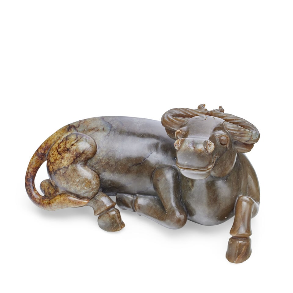 A large Chinese carved jade buffalo 19th/20th century: A large Chinese carved jade buffalo 19th/20th century Of dark grey green stone, shading to a paler tone with russet markings on its rear, the recumbent beast carved on all sides with the legs tucked u