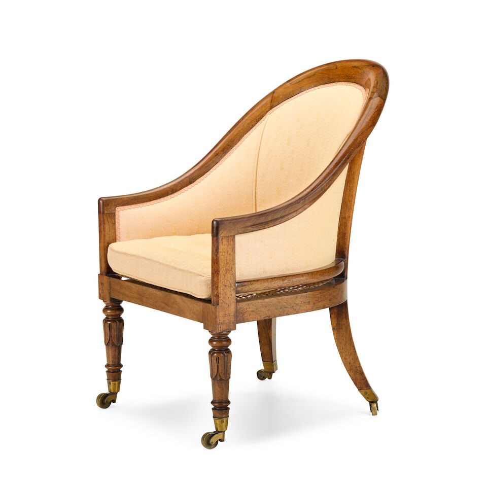 A George IV rosewood bergère Early 19th century: A George IV rosewood bergère Early 19th century Of tub shaped form, the padded upholstered back above a caned seat with squab cushion, on lotus carved and turned front legs and splayed back legs