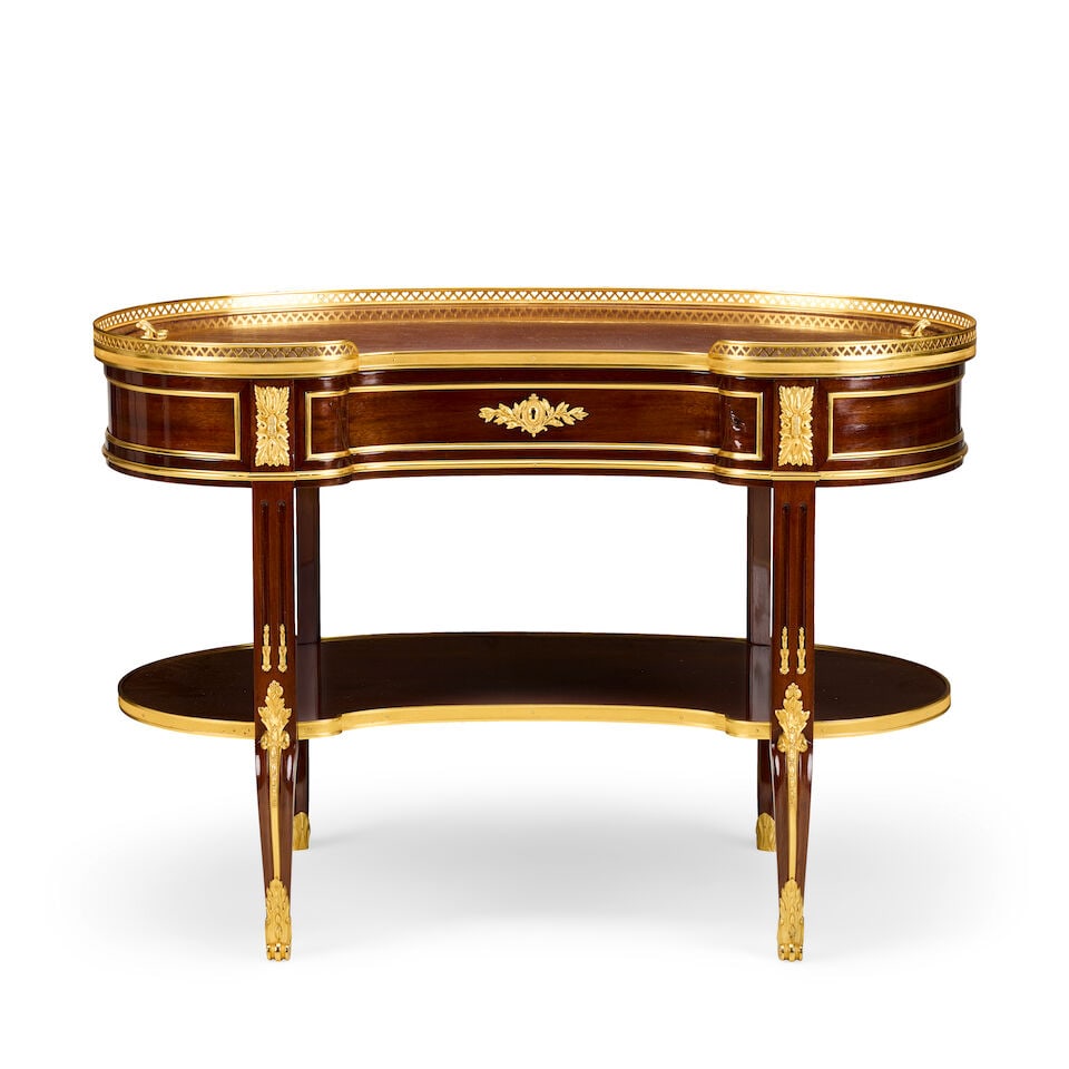 A French mahogany and gilt bronze mounted kidney shaped tableIn the Transitional style: A French mahogany and gilt bronze mounted kidney shaped table In the Transitional style The pierced heart-shaped three quarter gallery with a removable top enclosing a void interior above a panelled f
