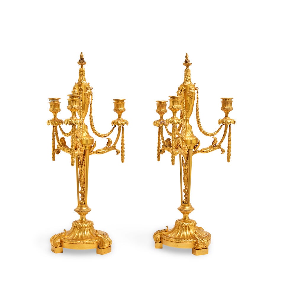 A pair of French late 19th century gilt bronze three branch candelabraIn the Louis XVI style (2): A pair of French late 19th century gilt bronze three branch candelabra In the Louis XVI style The central urns hung with trailing olive leaves connected to three scrolling acanthus leaf candle arms is