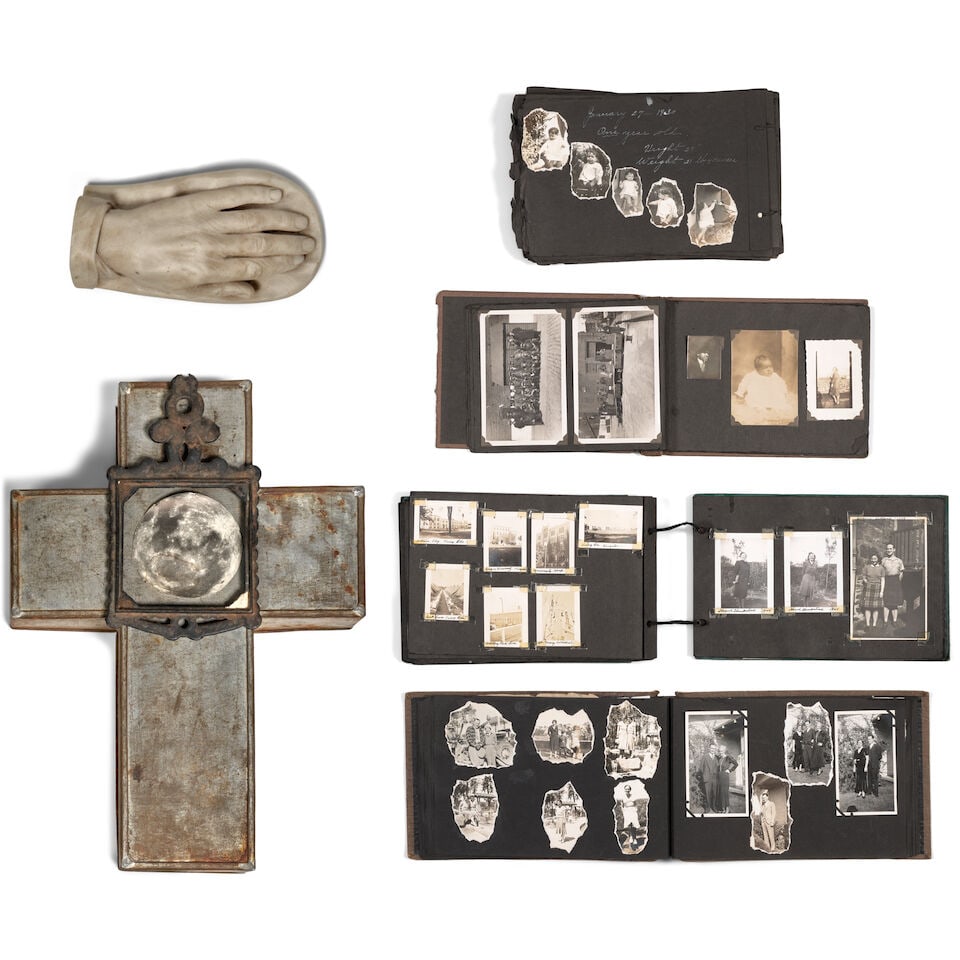 A CURATED GROUP OF TABLE DECORATIONS: A CURATED GROUP OF TABLE DECORATIONS Comprising four photo-albums, a carved alabaster hand, and a metal cross with a hand-placed image of a moon under a metal frame. length of cross