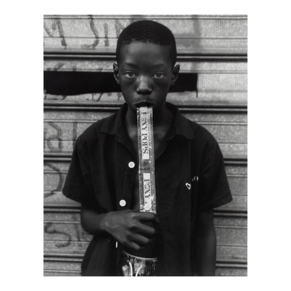 Dawoud Bey (born 1953); A Boy Eating a Foxy Pop, Brooklyn, NY;: Dawoud Bey (born 1953) A Boy Eating a Foxy Pop, Brooklyn, NY, 1988 Gelatin silver print, printed 1997; signed and dated in pencil on the reverse, framed. 12 3/4 x 10 in. (32.4 x 39.4 cm.) sheet 14 x 1