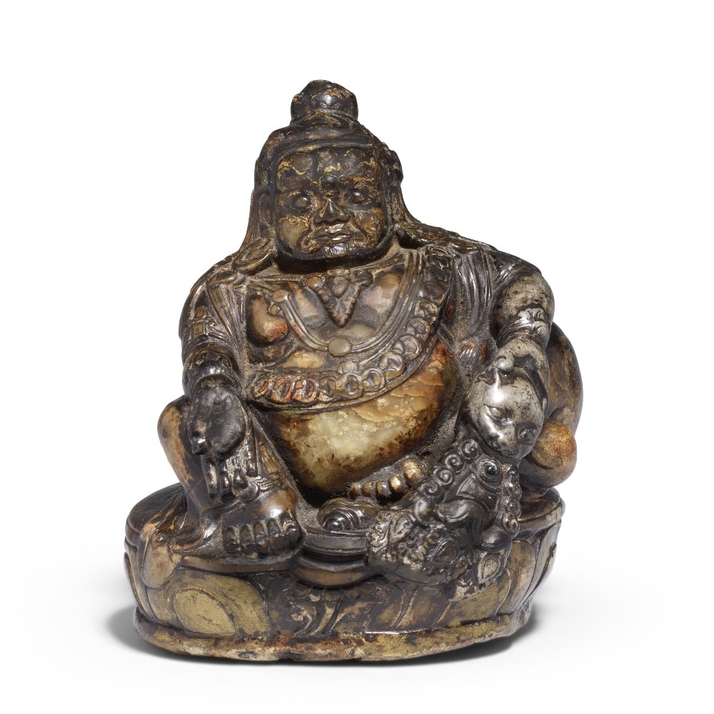 A VERY RARE SOAPSTONE FIGURE OF JAMBHALA: A VERY RARE SOAPSTONE FIGURE OF JAMBHALA Tibet, 17th century The deity finely carved seated in lalitasana on a lotus-petal base, the rotund belly resting atop his left foot before a conch shell and dr