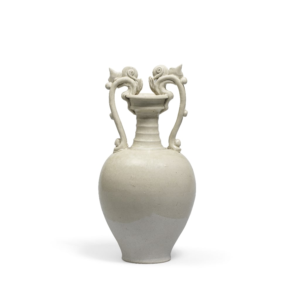 A WHITE-GLAZED AMPHORA Tang Dynasty: A WHITE-GLAZED AMPHORA Tang Dynasty The tapered ovoid body rising to a ribbed neck below the cupped mouth, with a pair of dragon-shaped handles biting the rim, covered with a greenish-beige glaze endi