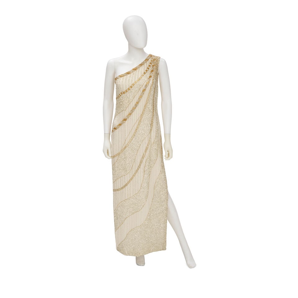 BOB MACKIE: WHITE AND GOLD BEADED ASYMMETRICAL GOWN 1970'S: BOB MACKIE: WHITE AND GOLD BEADED ASYMMETRICAL GOWN 1970'S • Marked Size 10 • Bugle Beaded Silk Chiffon Exterior • Zip Closure For further information on this lot please visit Bonham