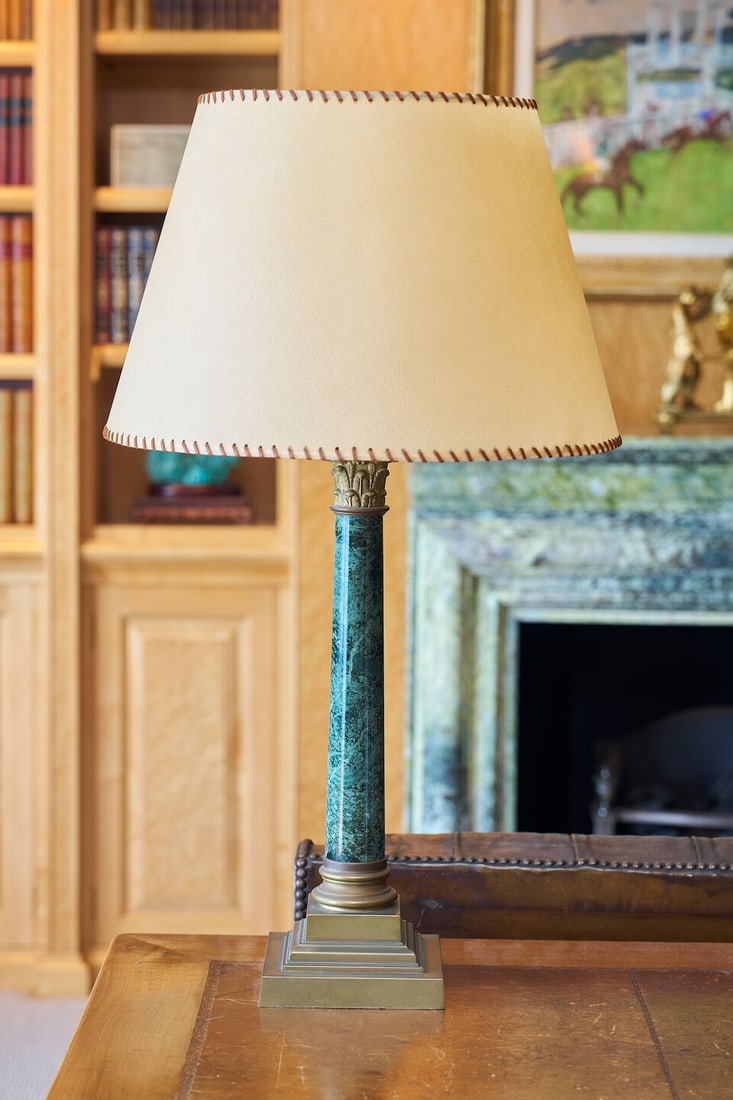A brass and green marble table lamp height: 76.0cm including shade: A brass and green marble table lamp with a Corinthian column top and stepped base, fitted with a simulant cream shade, height: 76.0cm including shade For further information on this lot please visit B