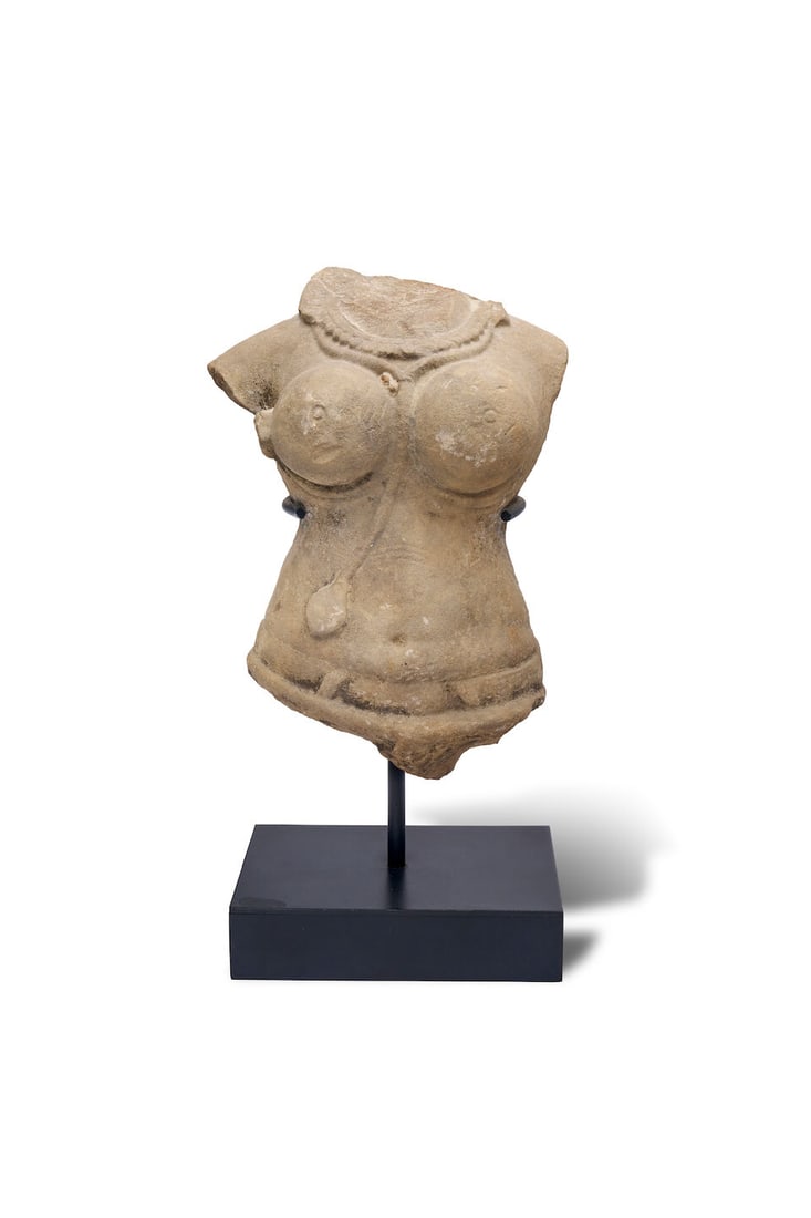 A sandstone torse of a female deity Indian, 10th century: A sandstone torse of a female deity Indian, 10th century with pronounced rounded breasts, an ornate beaded necklace, and a decorative waistband, mounted on a metal stand, 24.0cm high For further infor