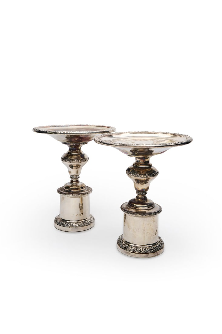 A pair of Continental presentation stands, 20th century,: A pair of Continental presentation stands, 20th century, each baluster form trimmed with repoussé borders of scrolling acanthus leaves, surmounted by a circular platter, in silver plate, height