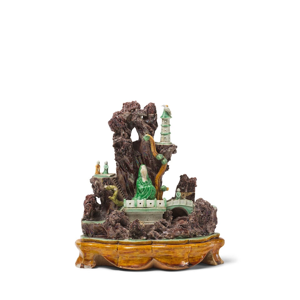 RARE GROTTE EN BISCUIT ÉMAILLÉ JAUNE, VERT ET AUBERGINE Dynastie Qing, époque Kan...: RARE GROTTE EN BISCUIT ÉMAILLÉ JAUNE, VERT ET AUBERGINE Dynastie Qing, époque Kangxi (1662-1722) A BISCUIT GROTTO WITH GUANYIN Qing Dynasty, Kangxi period Wood stand. 22.5 cm (8 7/8