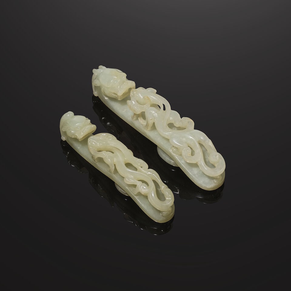 DEUX BOUCLES DE CEINTURE EN JADE CÉLADON SCULPTÉ Dynastie Qing, XIXe siècle (2): DEUX BOUCLES DE CEINTURE EN JADE CÉLADON SCULPTÉ Dynastie Qing, XIXe siècle TWO CELADON JADE BELT HOOKS Qing Dynasty, 19th century 12.2 cm (4 3/4 in.) and 10.5 cm (4 1/8 in.) long (2). 