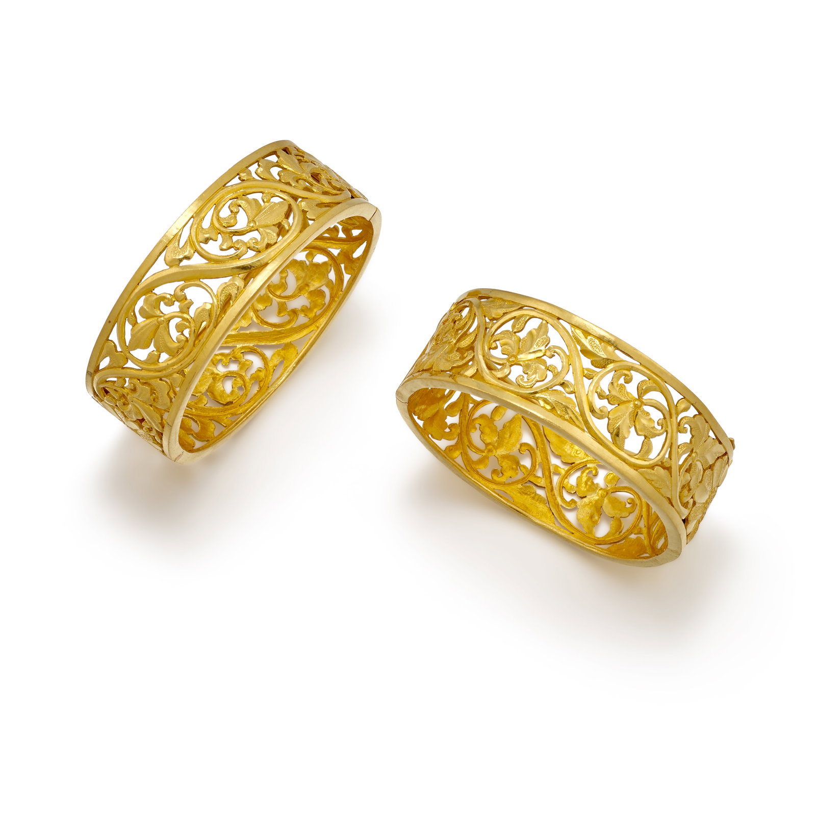 A PAIR OF GOLD BRACELETS: A PAIR OF GOLD BRACELETS Each hinged bangle of openwork, floral-motif design; each with maker's and/or assay marks; each fabricated in 23k gold; inner circumferences 6 in., widths 3/4 in. Footnotes: