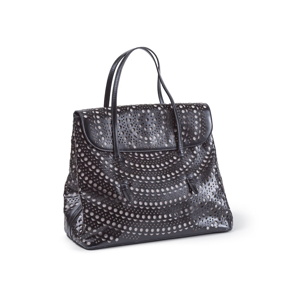 Alaia. Sac fourre-tout en cuir perforé noir sur fond écru. Alaia. Tote bag in perfora...: Alaia. Sac fourre-tout en cuir perforé noir sur fond écru. Alaia. Tote bag in perforated black leather on an ecru background. 36 x 30 x 17 cm. Footnotes: Très bon état