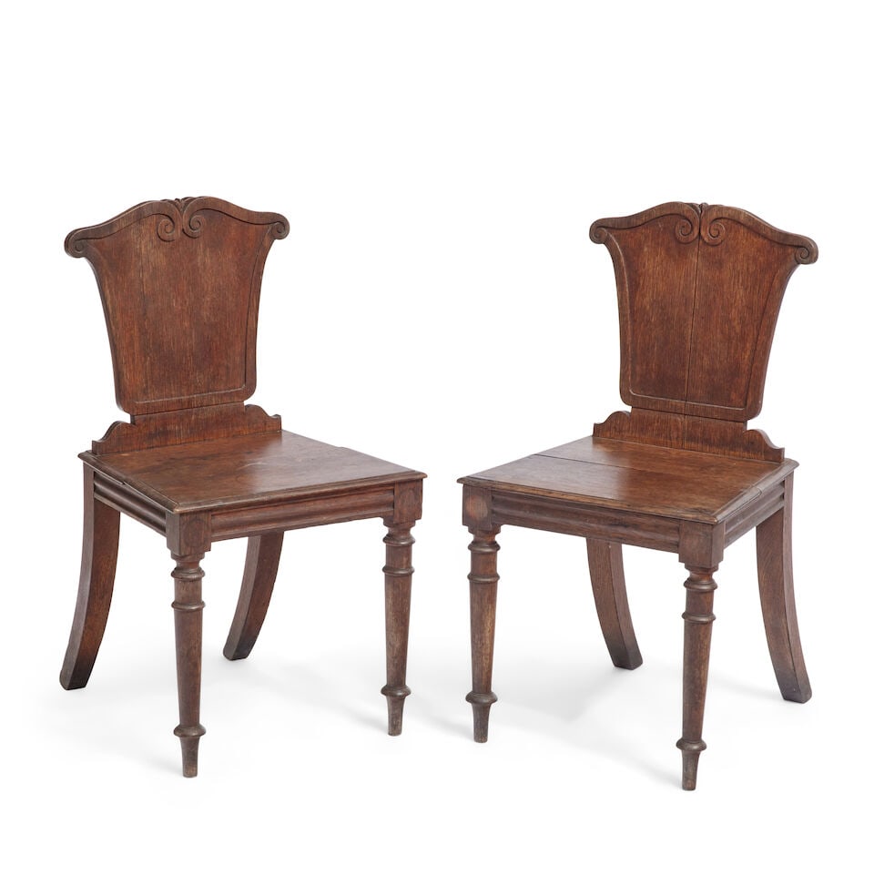 A pair of Regency oak hall chairs Second quarter 19th century (2): A pair of Regency oak hall chairs Second quarter 19th century Each with shaped back above solid seats raised on turned tapering front legs, 46cm wide x 52cm deep x 85.5cm high, (18in wide x 20in deep