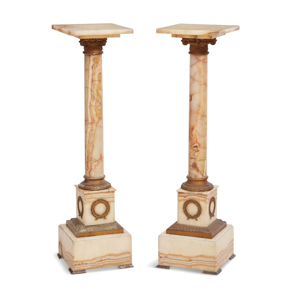 A pair of Onyx and gilt metal mounted column torchere stands Late 19th/ early 20th century in th...: A pair of Onyx and gilt metal mounted column torchere stands Late 19th/ early 20th century in the Empire style Of typical form, the square tops on turned supports surmounted by ionic capitals, the