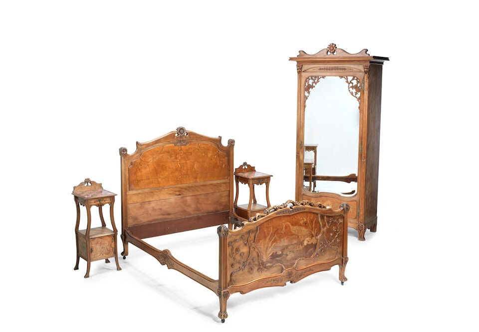 An Art Nouveau carved walnut and marquetry bedroom suite In the manner of Majorelle (5): An Art Nouveau carved walnut and marquetry bedroom suite In the manner of Majorelle (5) In the manner of Majorelle Comprising: a wardrobe, with shaped bevelled mirror, a double bed with shaped