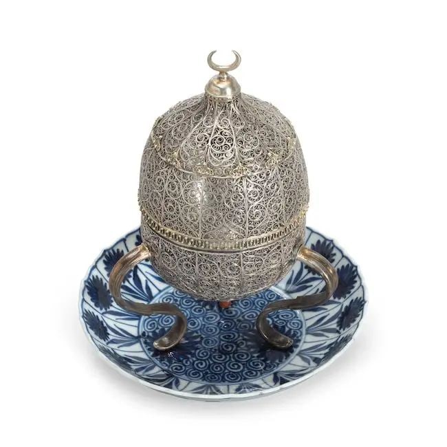 An Ottoman silver filigree incense burner mounted on a Kangxi porcelain dish Turkey and China, ...: An Ottoman silver filigree incense burner mounted on a Kangxi porcelain dish Turkey and China, late 17th/ early 18th Century of ovoid form with hinged lid on three curved feet, comprising panels of fi