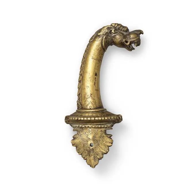 A brass hilt in the form of a makara head South India, possibly Tanjore, 18th/ 19th Century: A brass hilt in the form of a makara head South India, possibly Tanjore, 18th/ 19th Century the ricasso of foliate form, makara head quillons in the form of makara masks, the grip in the form of a lon