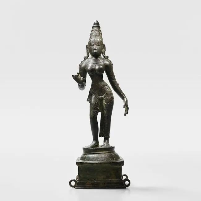 A copper alloy figure of Parvati Tamil Nadu, Chola Period, circa 11th Century: A copper alloy figure of Parvati Tamil Nadu, Chola Period, circa 11th Century standing in tribhanga on a lotus pedestal, wearing a closely-fitting dhoti tied with a sash at the waist, her left arm in 