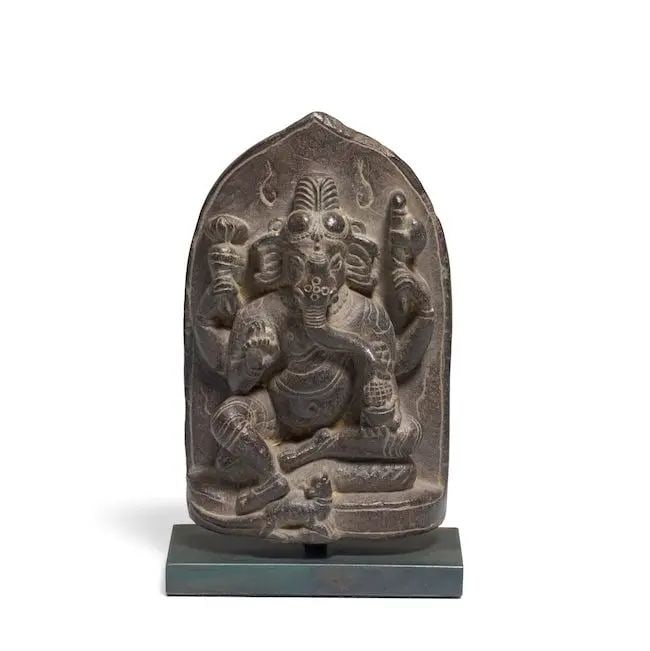 A black stone figure of Ganesh North East India, 11th/ 12th Century: A black stone figure of Ganesh North East India, 11th/ 12th Century Ganesh is seated in royal ease, his pendent foot resting on his vehicle, the rat, his four arms holding a radish, axe, rosary and bo
