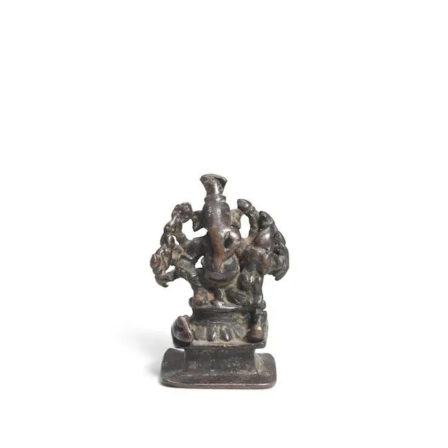 A bronze figure of Ganesh India, 16th Century: A bronze figure of Ganesh India, 16th Century on a square pedestal surmounted by a lotus throne, flanked by bandicoots, his consort on his left knee 8.5 cm. Footnotes: Provenance Private UK collection