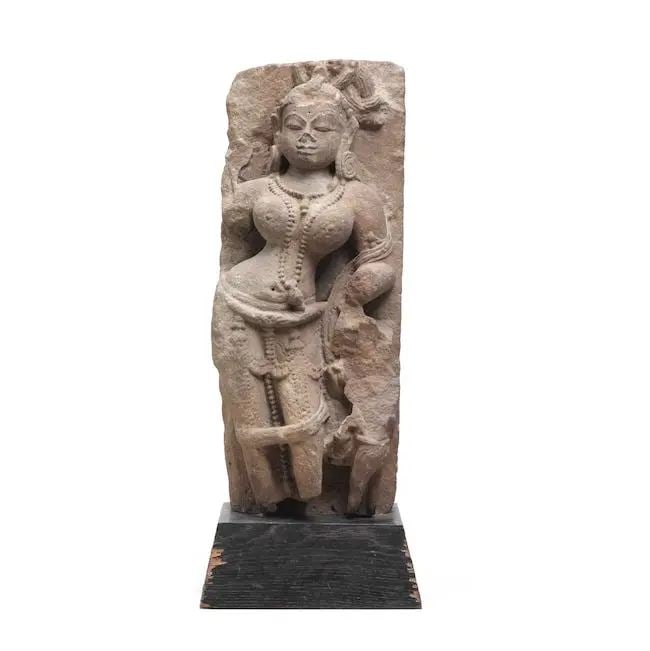 A sandstone figure of a celestial beauty (Surasundari) North India, 10th/ 11th Century: A sandstone figure of a celestial beauty (Surasundari) North India, 10th/ 11th Century carved in deep relief and stylistically with exaggerated contortion to torso and prominent breasts, shawl to shou