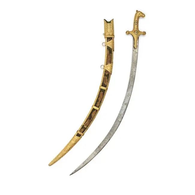 A Kutch gilt-copper horsehead-hilted sword Western India, early 19th Century: A Kutch gilt-copper horsehead-hilted sword Western India, early 19th Century the single-edged steel blade of curved form, the hilt decorated in repoussé and chased with floral interlace, horsehea