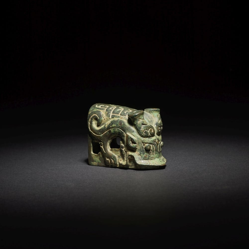 PETIT ORNEMENT DE HARNAIS EN BRONZE Fin de la dynastie Shang (2): PETIT ORNEMENT DE HARNAIS EN BRONZE Fin de la dynastie Shang A SMALL ARCHAIC BRONZE FITTING Late Shang Dynasty Of hollow rectangular section, terminating in a horned dragon head with protruding horns,
