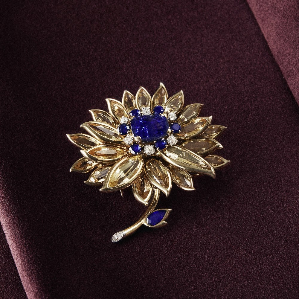 CARTIER: SAPPHIRE, TOPAZ AND DIAMOND FLORAL CLIP, CIRCA 1945: CARTIER: SAPPHIRE, TOPAZ AND DIAMOND FLORAL CLIP, CIRCA 1945 The stylised dahlia, centred by a cushion-shaped sapphire weighing 12.03 carats, within a circular-cut sapphire, old brilliant and old cush